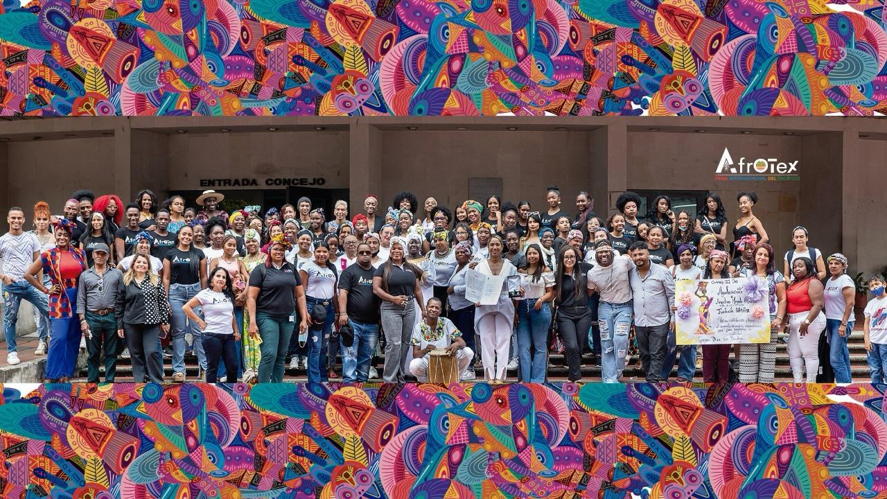 Foto grupal de más de cien integrantes de la comunidad Afrotex en las escaleras de la entrada del Concejo de Cali, enmarcada por un mural de colores